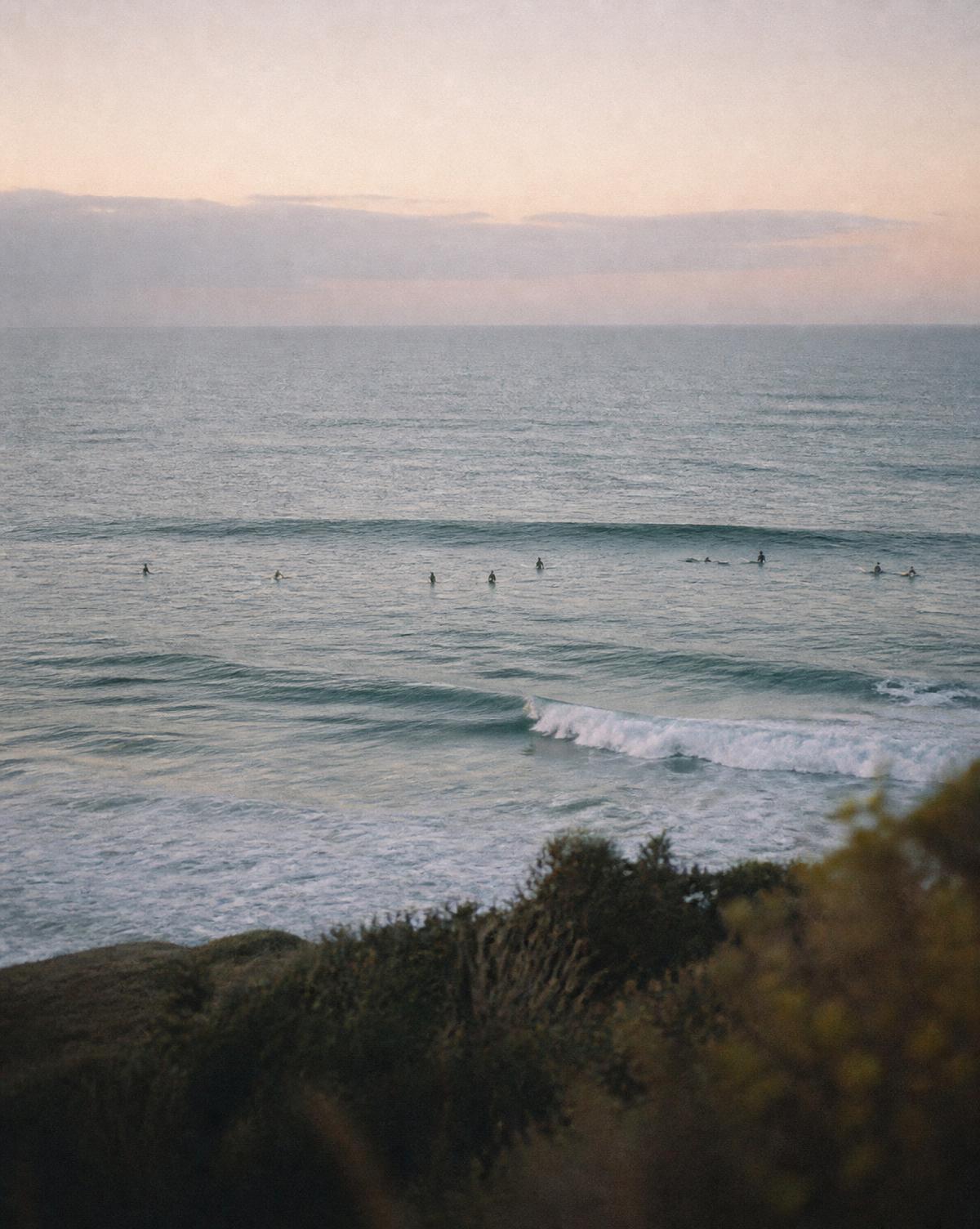 Surfers and swimmers in soft dawn light at a beach break